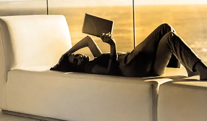 Woman lying on a sofa beside window reading magazine