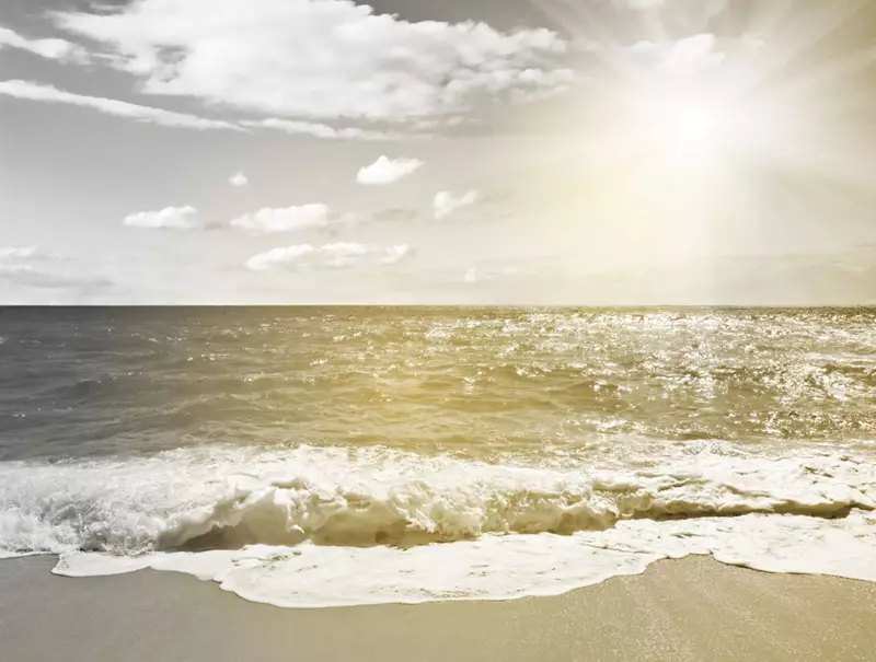 Image of beach with the sea waves crashing and sun in top left corner