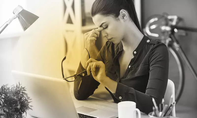 Woman suffering from digital eye strain, holding her head in her hands 