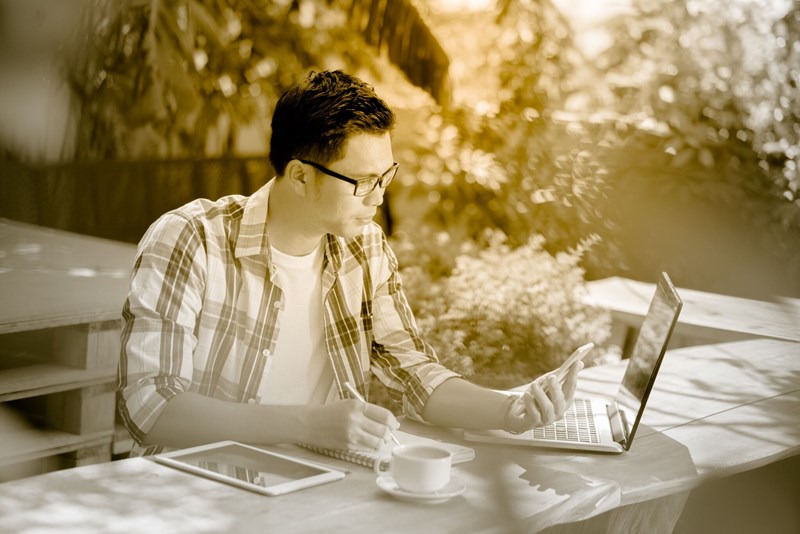 Male working outdoors on mobile and laptop wearing eyeglasses