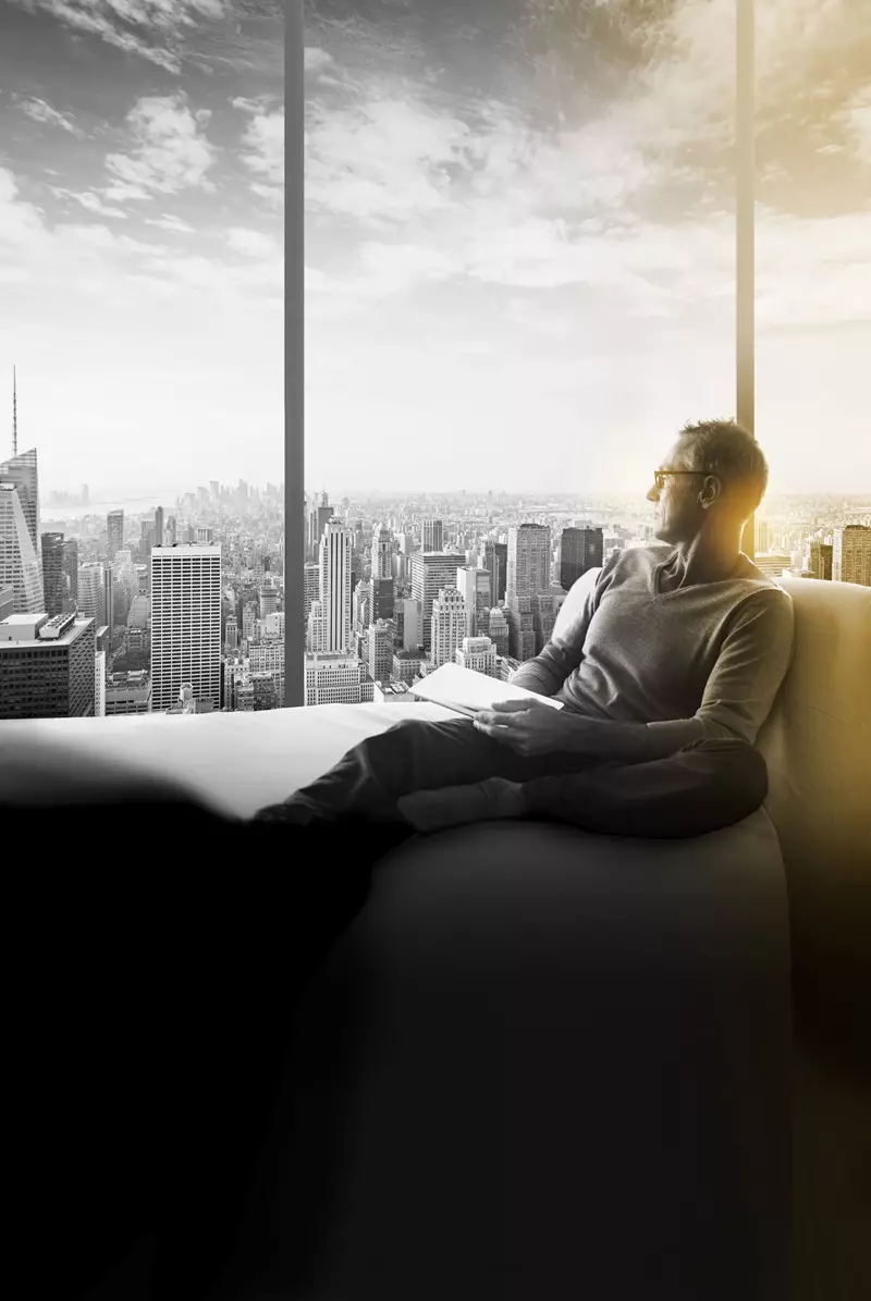 Male wearing eye glasses sitting on sofa looking out of skyscraper window 