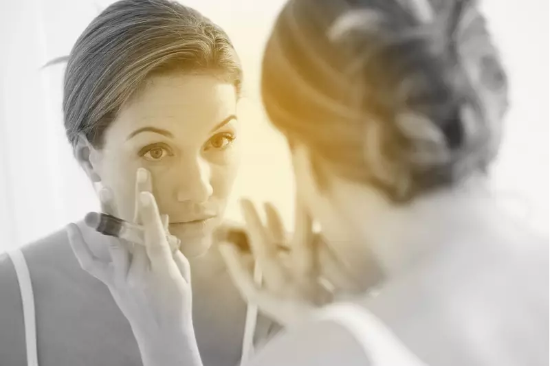 Woman applying concealer with her finger in a mirror 