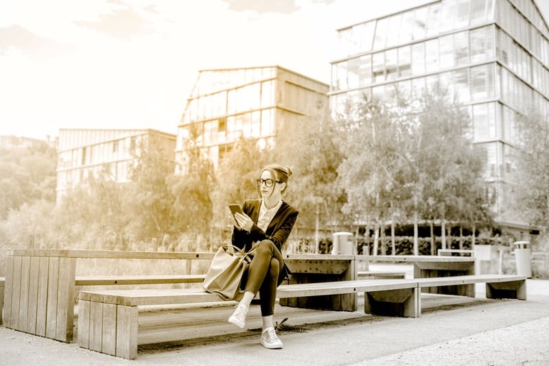 Female outdoors sitting on park bench wearing glasses using smartphone