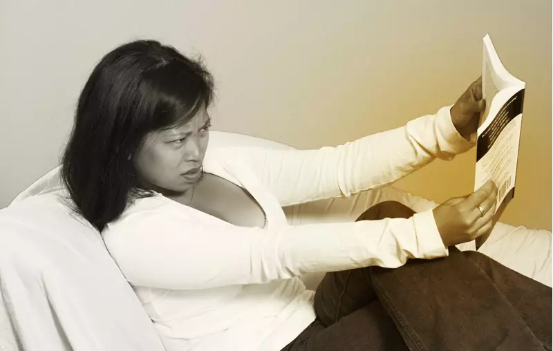 Woman holding magazine far away from her face as she is struggling to read up close