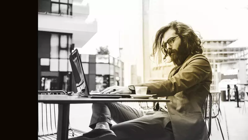 Male wearing glasses sitting at outdoor table on a laptop