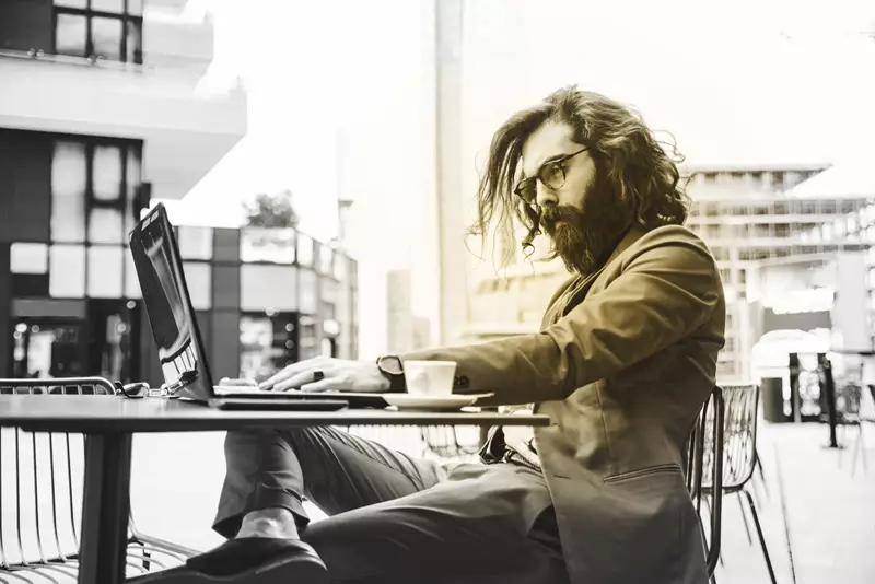 Male wearing glasses sitting at outdoor table on a laptop