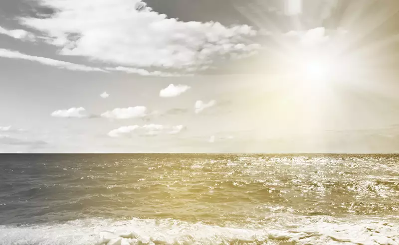 Image on a beach with the sea waves and the sun glaring down