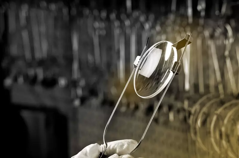 Person holding lens in a clamp for inspection