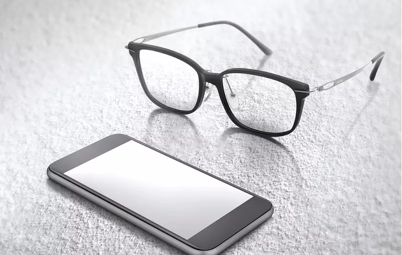 Spectacles sat on surface beside smartphone