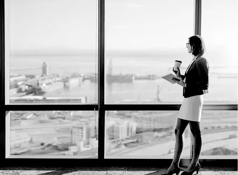 Female wearing eyeglasses holding coffee cup and tablet looking out of window