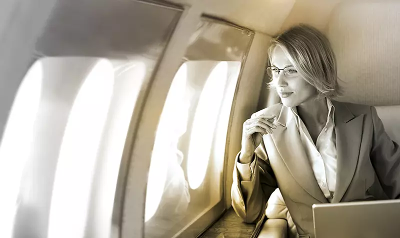 Female on flight wearing eyeglasses looking out of window with laptop in front of her