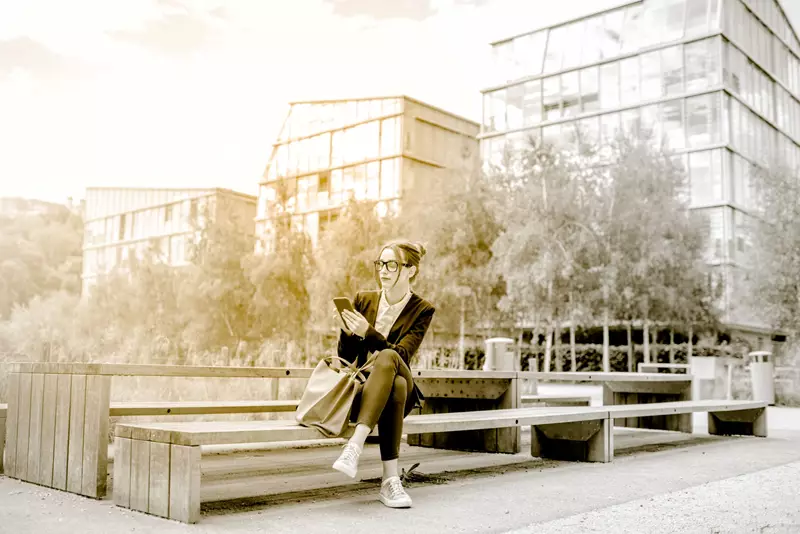 Female sitting outside on park bench wearing glasses on smartphone