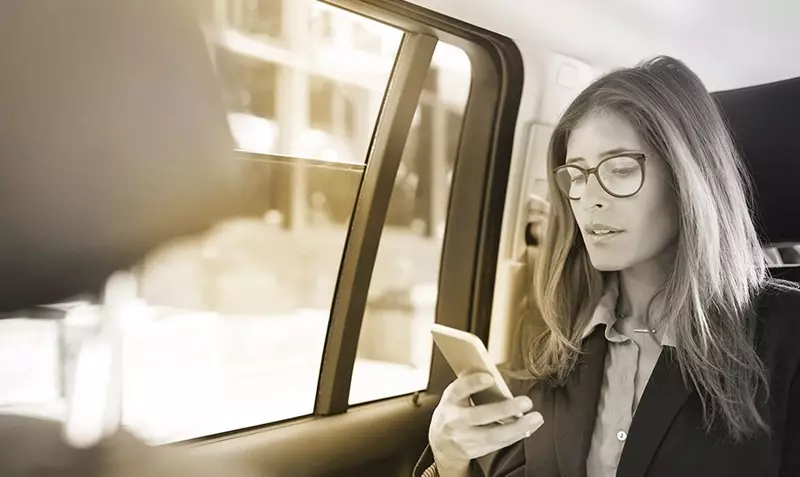 Female in back seat of car wearing glasses using smartphone
