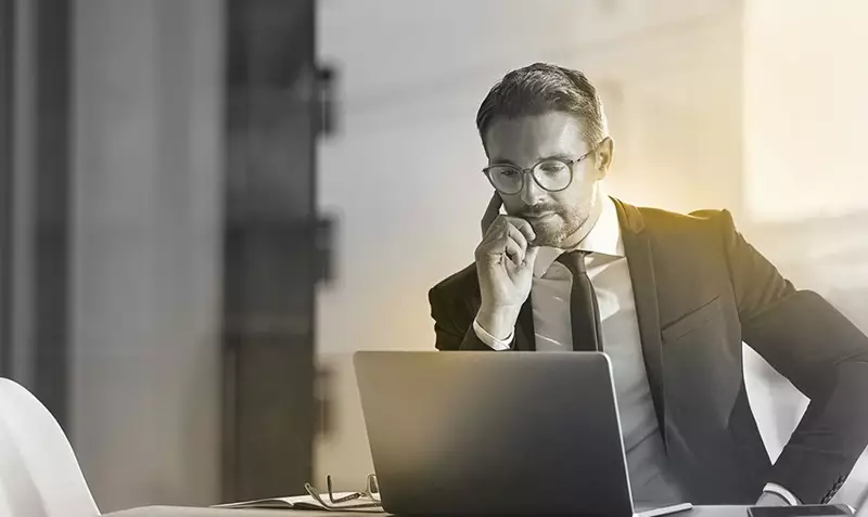 Male wearing eyeglasses working behind laptop screen