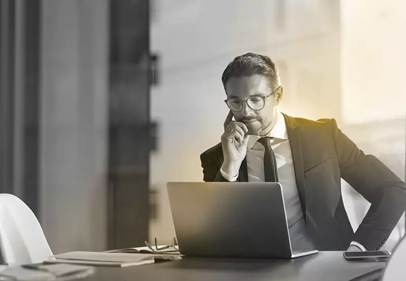 Male business man wearing glasses on phone call behind a laptop screen