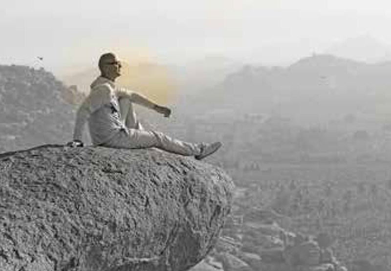 Male wearing glasses sitting on top of a rock
