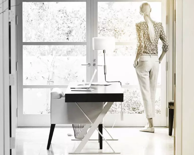 Female standing up staring out of a window behind a desk 