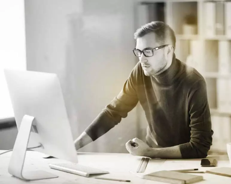 Male wearing eyeglasses working inside behind a computer screen